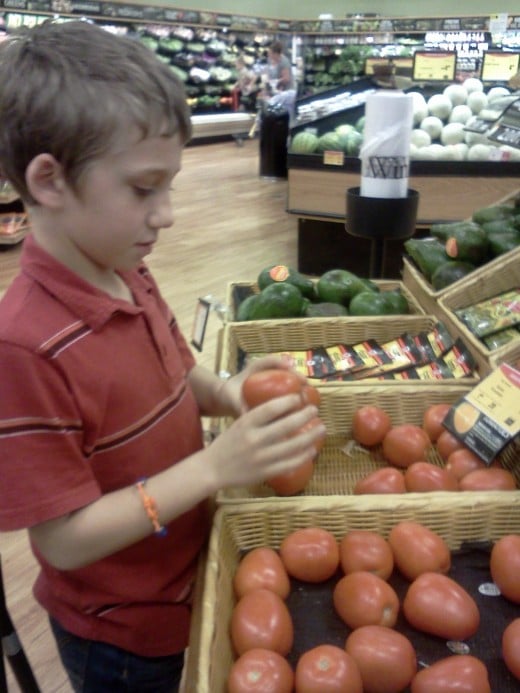 Invite your children to menu plan, make shopping lists.  Here, my oldest son looks for bruising on a tomato.  We know organic and home grown taste the best and offer the greatest nutritional value.
