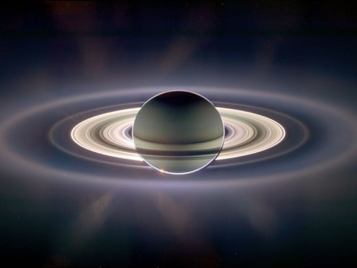 The backside of Saturn, eclipsing the sun. The reflection of sunlight off the rings is so bright that it illuminates the planet's night side. Above the main rings on the left is a tiny blue dot (as Carl Sagan called it): Earth. 