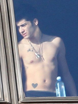 Zayn Malik is topless as he looks outside the hotel window where One Direction stayed while in Australia. Some of his tattoos including the one of the heart on the stomach are clearly visible. 
