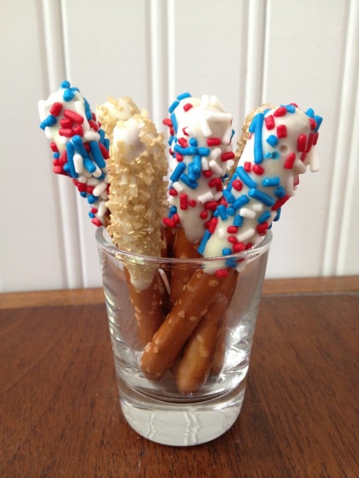 Small pretzel dipping sticks dipped in white chocolate; red, white & blue jimmies; and gold sugar gems