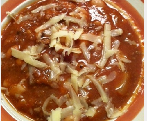 A delicious piping hot bowl of chili with shredded cheese.