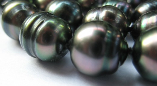 A close-up picture of a few of a necklace of baroque peacock Tahitian pearls. The lustre and colour on these are wonderful, and the surface smooth with a few pits. They are approximately 9 to 10mm in size.  (c) A Jones 2012