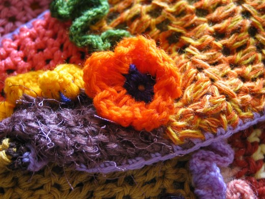 DESCRIPTIONCloseup of an orange crocheted flower with a multi-colored crochet fabric background. 