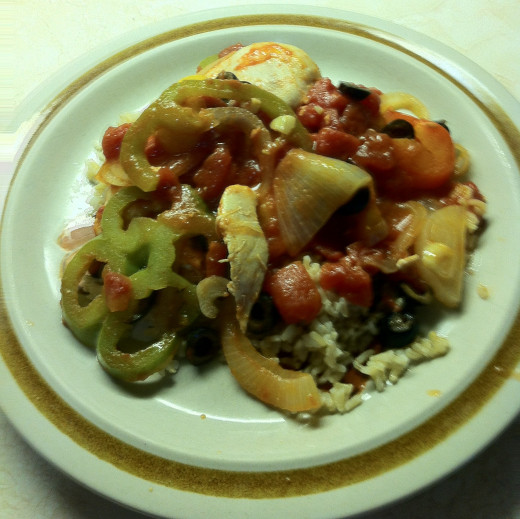 Chicken breasts smothered in tomatoes, peppers, garlic and onions on top of a bed of rice with black olives.