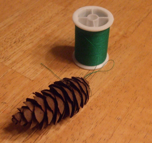 Thread slips under scales at the top of the clean pine cone.