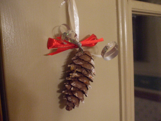 The finished pine cone ornament hanging on a door.
