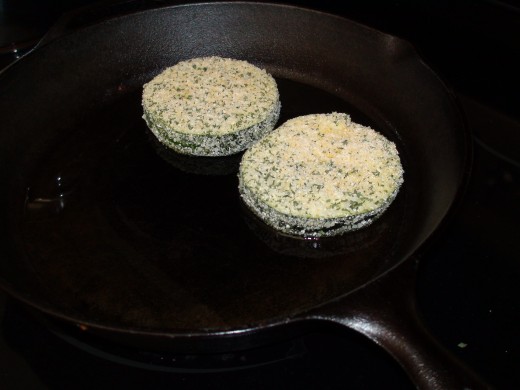 Zucchini coated in egg and bread crumb mixture, placed in preheated cast iron pan.