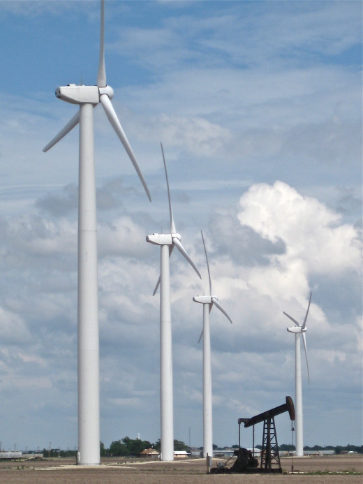 Wind turbines contrast with a nearby oil derrick to show the old and new ways of creating power.