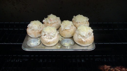 Stuffed mushrooms sitting in a small cup muffin tray on the top rack of the barbecue.