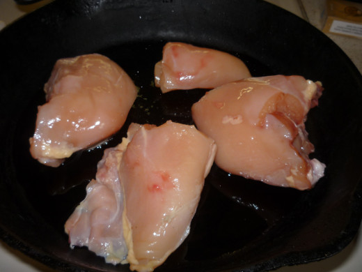 Fresh, skinless, bone in chicken breast in the skillet beginning the browning process.