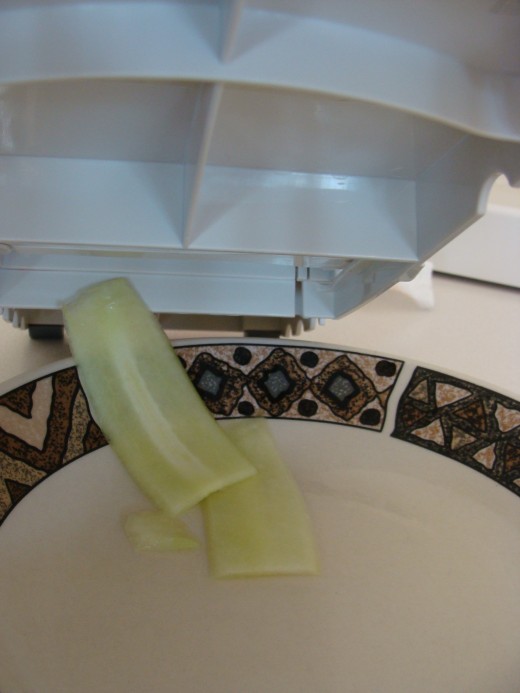 Vegetable slices come out from the bottom of the slicer and are uniform in thickness.