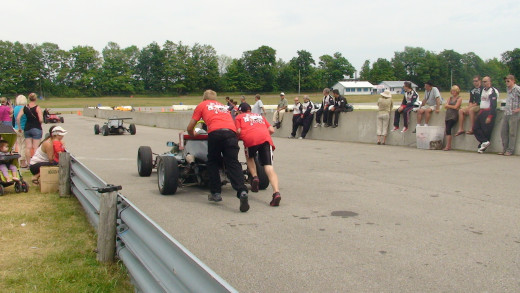 Giving the formula one car and driver a push towards the track.
