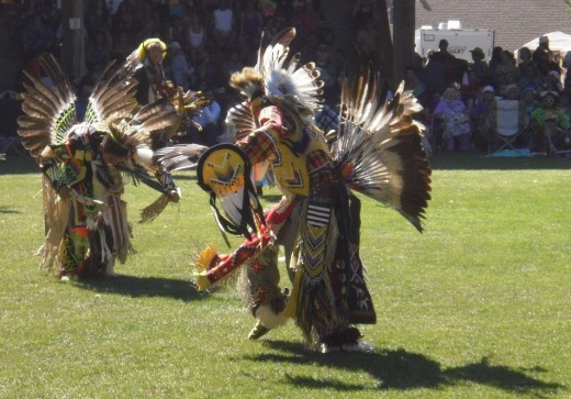 Men dancing in traditional regalia with eagle feather bustles, headdress and fans.