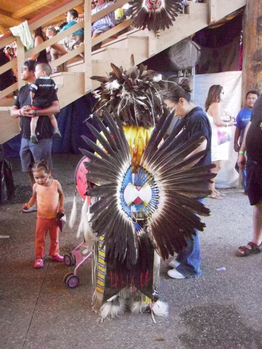 After the dance, young dancer finds his family.  His bustle and headdress are Eagle feathers.  In Canada, eagles are protected birds, and only First Nations people are allowed to possess them without heavy fines.