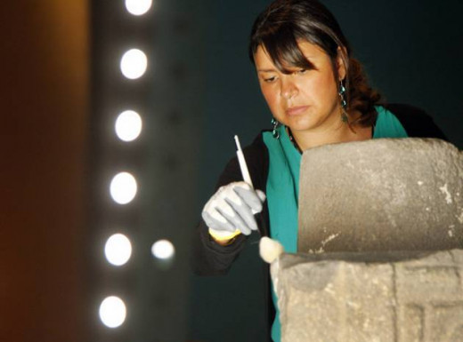 Visiting curator Alehandra Barajas brushes fragment of plumed serpent column during installation.