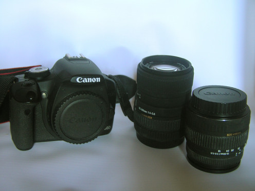 A DSLR camera body and two different lenses.