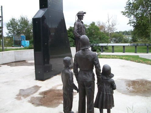 The Family sculpture, dwarfed by the larger-than-life statue of the Miner, at the Porcupine Miners' Memorial, Schumacher, Timmins