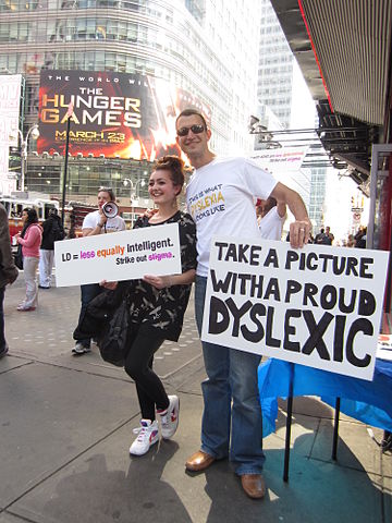 A girl poses for a photo in Times Square with a man holding a sign that says "Take a picture with a proud Dyslexic". The event was held to raise awareness of Learning Disabilities Month, by Project Eye-To-Eye.