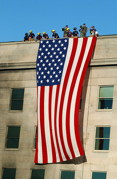 Soldiers from the 3rd Infantry render honors as fire fighters and rescue workers unfurl a huge American flag over the side of the Pentagon as rescue and recovery efforts continued following the September 11, 2001 terrorist attack. 