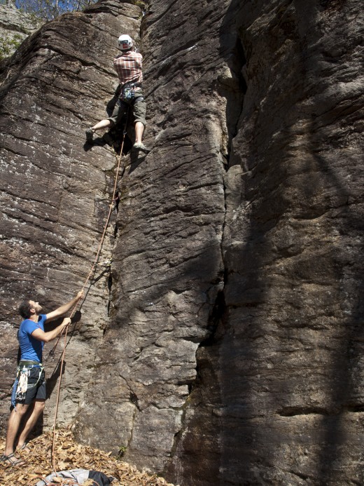 In this picture the climber is lead climbing, and the climber clips into protection as he climbs up the cliff. Instead of taking up slack as in a traditional top rope system, the belayer gives the climber slack.