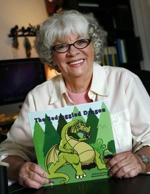 Diane Purdy is holding a copy of her children's book, Bedraggled Dragon