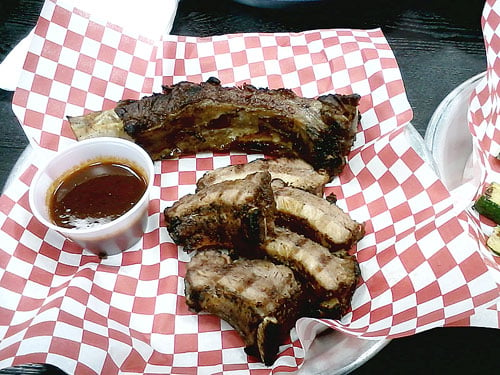 Beef rib near the top. Pork ribs near the bottom. Barbecue sauce in the cup to the left.
