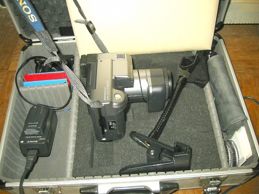 Sony Mavica-91 camera in its carrying case. To the right is a camera holder that can clamp onto a tabletop. To the left are batteries, battery charger, and a set of 3.5-inch floppy disks