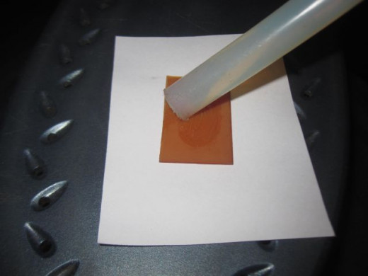 Melt hot-melt glue unto a rigid surface using a clothes iron as a heat source.