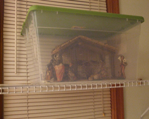 A Christmas Nativity set up inside a plastic storage container on a high shelf to protect it from pet cats.