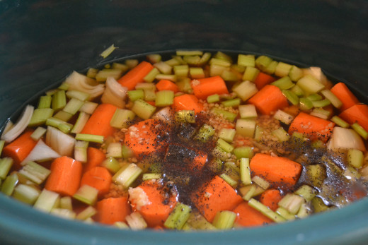 Start by chopping the vegetables and placing them in the bottom of your slow cooker along with two cans of beef broth.