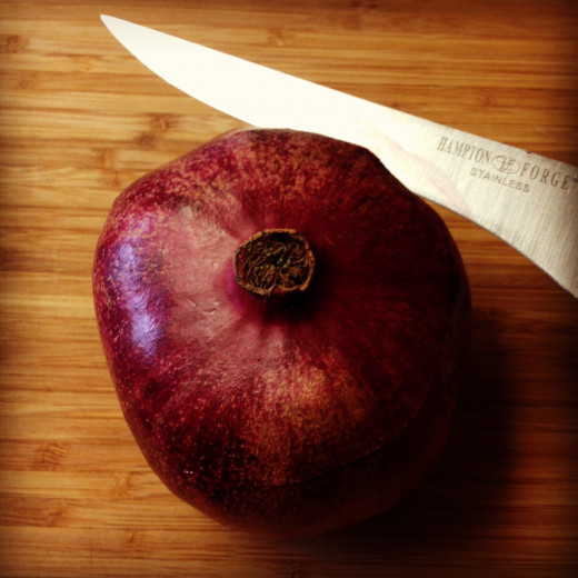 The first thing you'll want to do is use your knife to score the pomegranate about a 1/3 of the way down. You don't want to go too deep. Just cut through the skin (not the seeds).