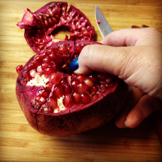 Hold your pomegranate in both hands  (I had to use the camera). Using your thumbs in the center gently pull the pomegranate apart.