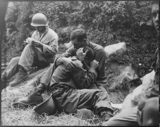 A grief stricken American infantryman whose buddy has been killed in action is comforted by another soldier. In the background a corpsman methodically fills out casualty tags, Haktong-ni area, Korea.