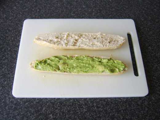 Mashed avocado is spread on the bottom half of the baguette