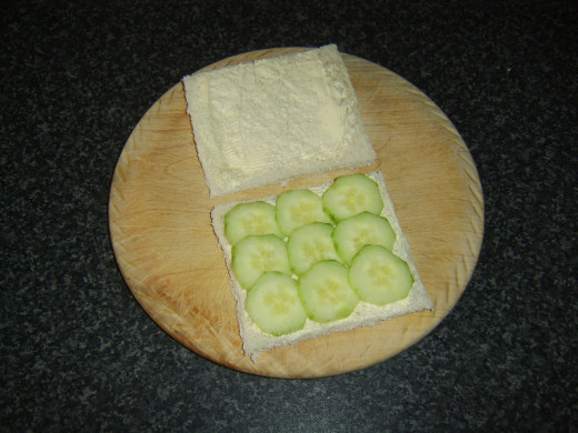 Cucumber slices are laid on one slice of the buttered bread