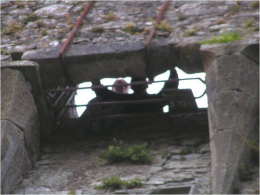 This shows a person lying on his back and being held down while being pushed out to kiss the underside of the Blarney Stone.