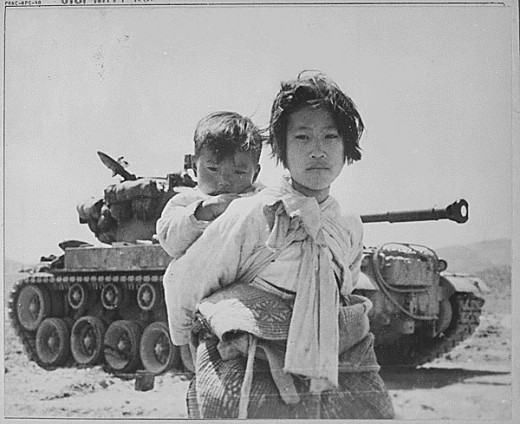 A Korean girl carries her brother past a stalled U.S. tank near Haengju, Korea, June 1951