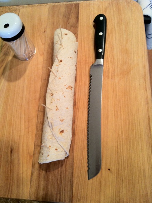 One complete tortilla roll ready for slicing into individual pieces using a serrated knife.
