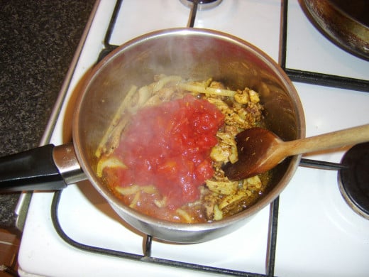 Canned tomatoes are added to spiced pork and onion