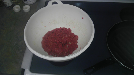 In a large mixing bowl are the ground beef, eggs, bread crumbs, diced onions, salt and pepper, and bleu cheese crumbles.