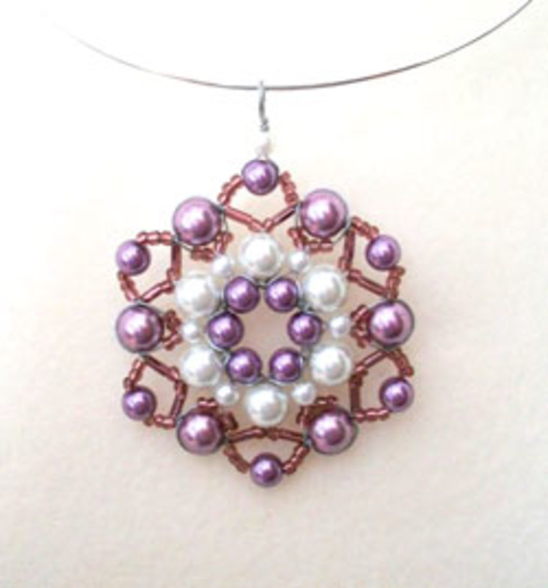 A purple beaded pendant using pearls in natural looking colours. 