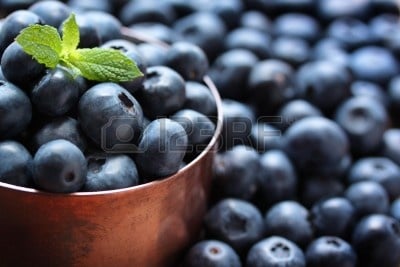 Blueberries in cooper tin. This is a great picture of Blueberries in a copper tin. And surrounded by Blueberries that are loose and just lying around.