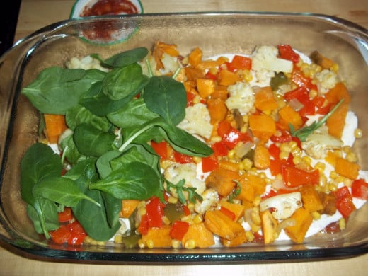 After the majority of the vegetables are roasted, the casserole is assembled in a second dish, here the spinach is added to the veggie layer. 