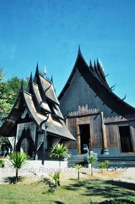 The main house of the dark Baan Dam is a large wooden structure with a multi-tiered roof that has protruding spikes that look like devil's horns.