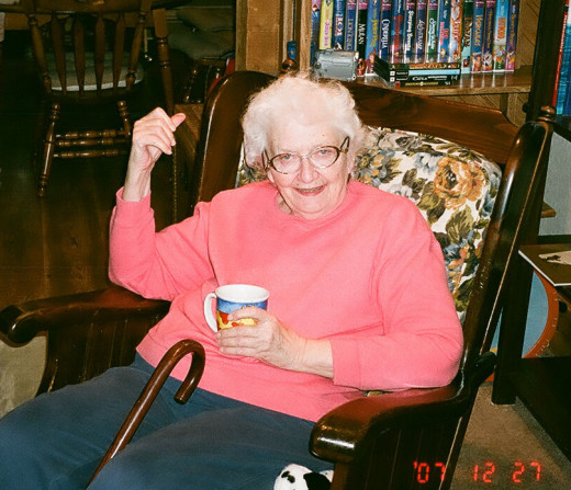At home in a wooden rocking chair with a cup of tea.  With family.   