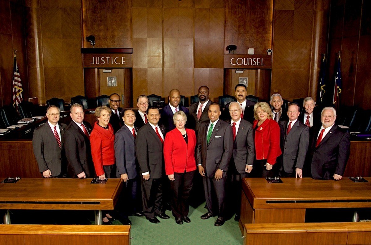 2014 photo of the Houston City Council with Mayor Annice Parker center in red jacket and pearls. These administrators have outlawed poor people from within the Houston city limits and likewise, charities or people from giving poor people food.