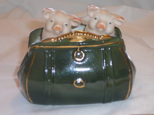 Two pigs in a Gladstone Bag. This fancy little bag has gilt buttons and clasp. It features straps while other versions are quilted and some have bears. 4 1/2" x 3 1/4". Paid $41. Common.
