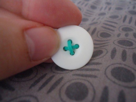 Here is what my button looked like when I inserted 2 broken bands through the holes. I wanted to mimic the look of a button so I made the bands form an X.