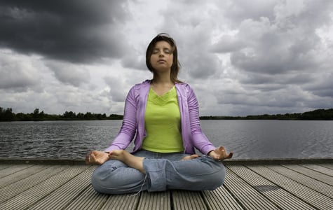 Woman doing meditation in the yoga posture known as full lotus, lotus pose or lotus position. Her left knee is supposed to be resting on the floor.