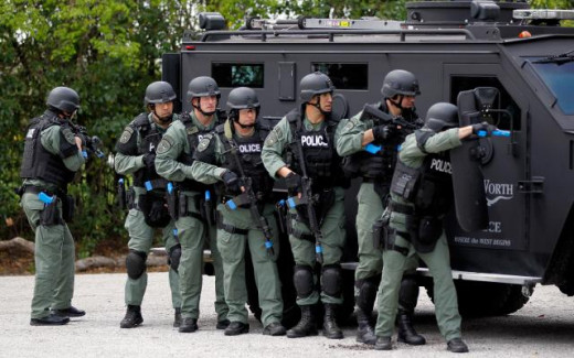 A SWAT team using an armored vehicle as cover.